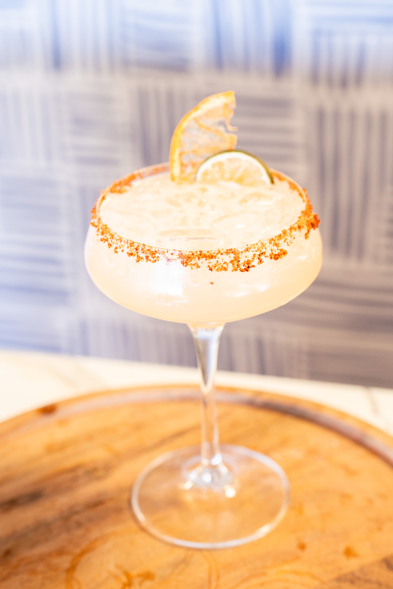 Spicy margarita in a coupe glass with chili rim, dried orange and lime
