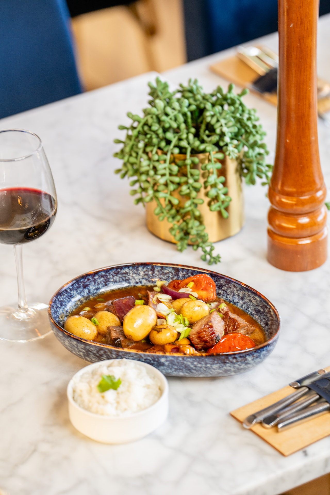 Lomo saltado in a blue bowl with white rice and a glass of red wine
